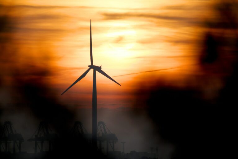 Harbor cranes and a wind turbine are seen as the sun sets in Bremerhaven in northern Germany, on Oct. 19, 2017. Credit: Patrik Stollarz/AFP via Getty Images