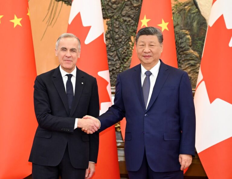 Chinese President Xi Jinping and Canadian Prime Minister Mark Carney shake hands while smiling at the camera, their country's flags behind them.