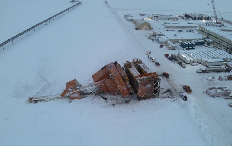 An aerial photo shows the oil rig collapsed in the snow next to a snowy road, emergency vehicles and an industrial complex