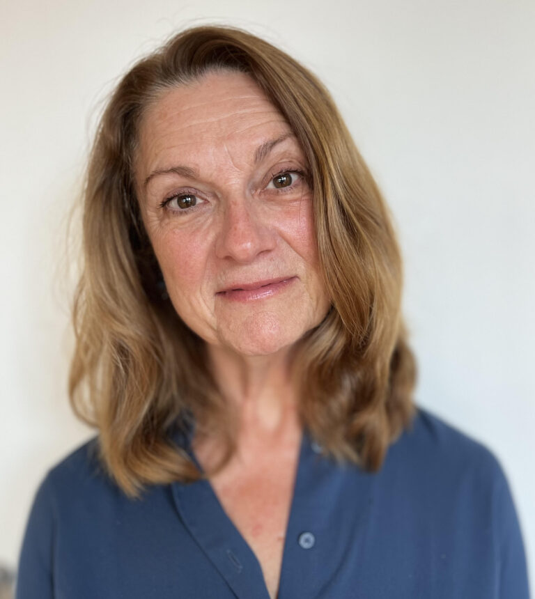 In a headshot photo, Christine Spolar is smiling at the camera. She has shoulder-length light brown hair and is waring a blue shirt.