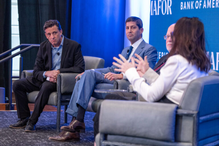 Kevin Warsh is sitting on a stage between several people