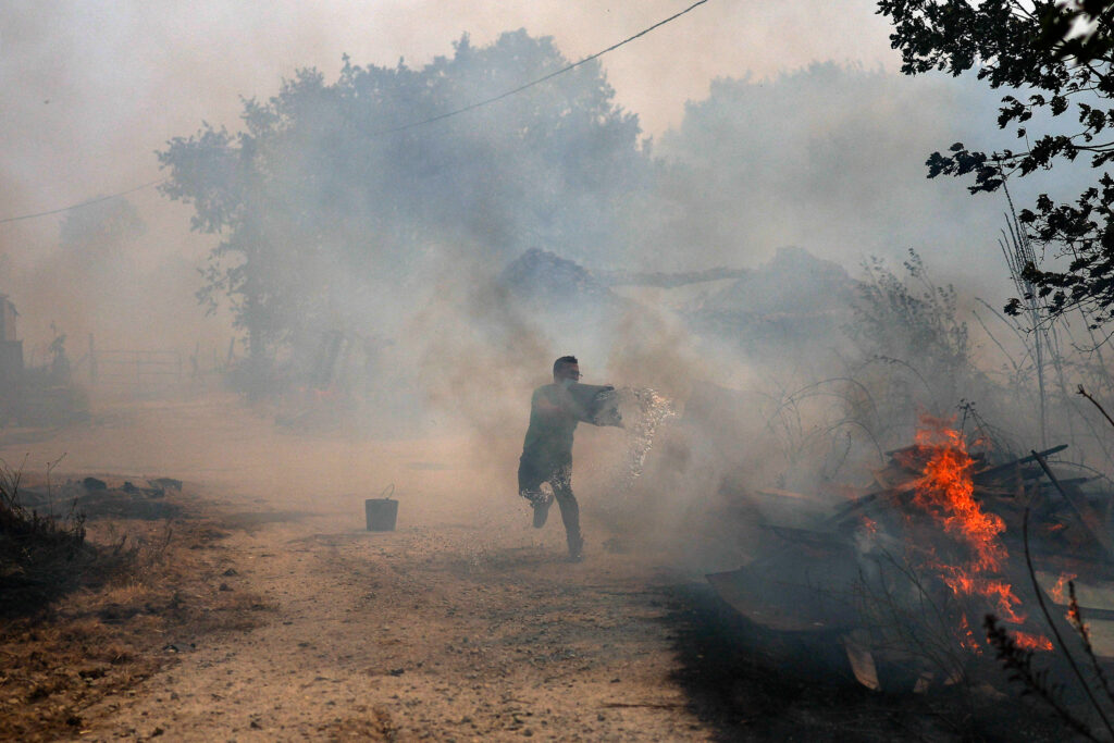 A man uses buckets of water to extinguish a wildfire that threatens his house in the Portuguese village of Antas on Aug. 15, 2025. Credit: Patricia de Melo Moreira/AFP via Getty Images
