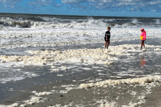Des gens pataugent dans l’écume de mer contaminée par les PFAS à Holden Beach, en Caroline du Nord, en octobre 2022. Crédit : Clean Cape Fear