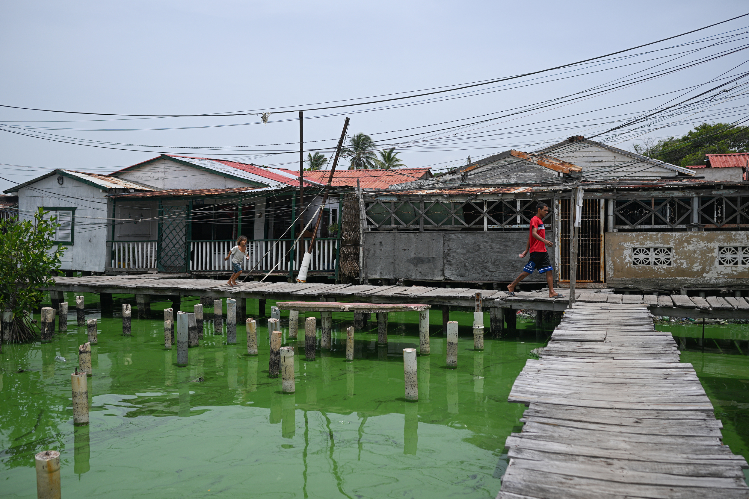 Des gens passent devant des maisons sur pilotis dans le quartier de Santa Rosa de Agua à Maracaibo, au Venezuela, alors qu'une nappe de pétrole recouvre les rives du lac Maracaibo le 11 juillet 2024. Crédit : Federico Parra/AFP via Getty Images