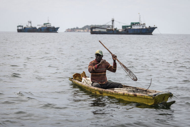 A fisherman paddles in front of commercial fishing boats off the coast of Dakar, Senegal. Credit: John Wessels/AFP via Getty Images